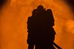 Silhouetted firefighter carrying person against fire — propane emergency training 2023
