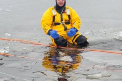 Person in yellow jacket sitting on wet shore — ice rescue training 2023