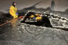 Person in yellow jacket standing on frozen ice next to hole — ice rescue 2024
